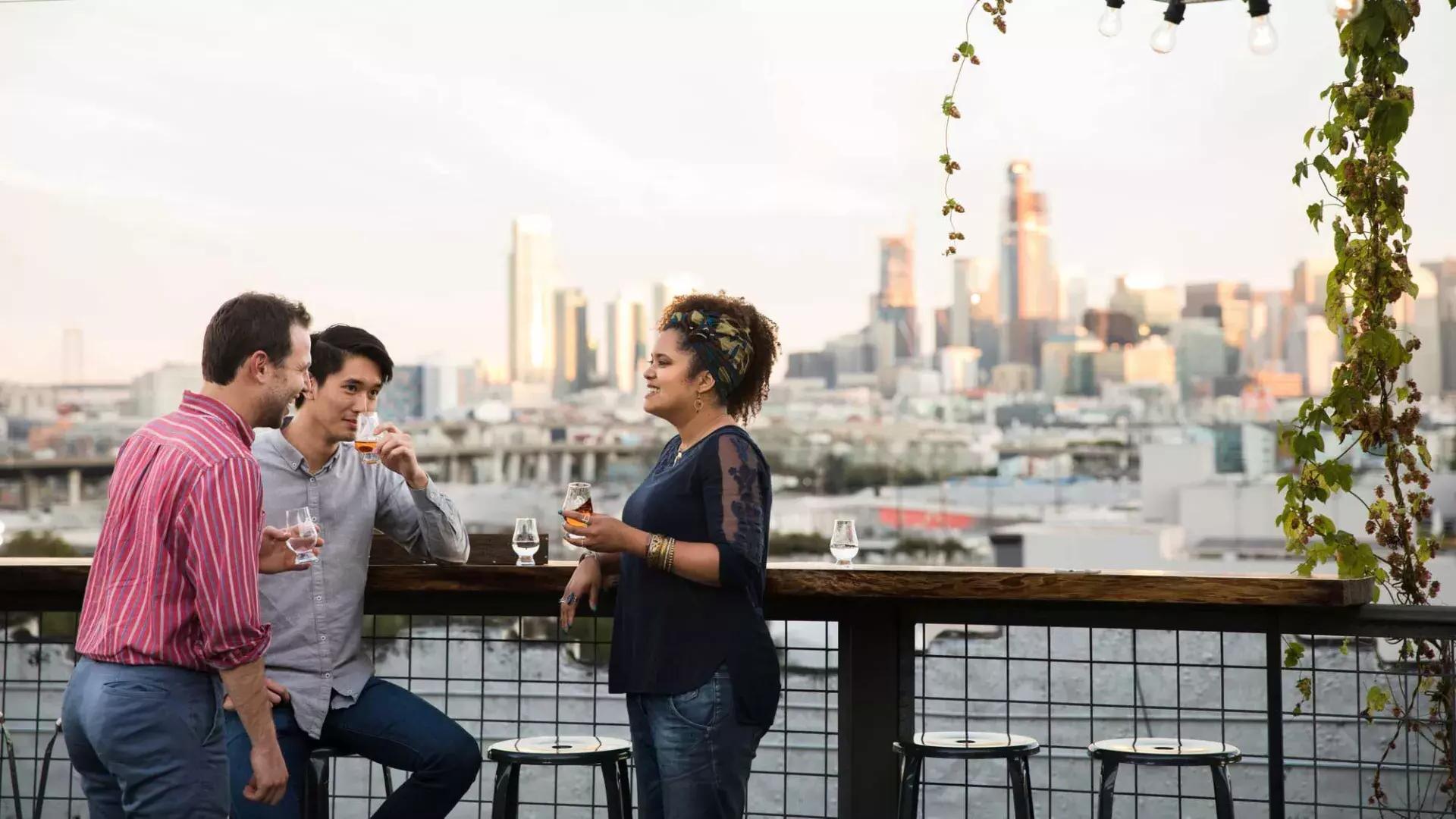 캘리포니아주 샌프란시스코에 있는 Anchor Distilling의 옥상 데크에 있는 야외 테이블 주위에 세 사람이 모여 있습니다.