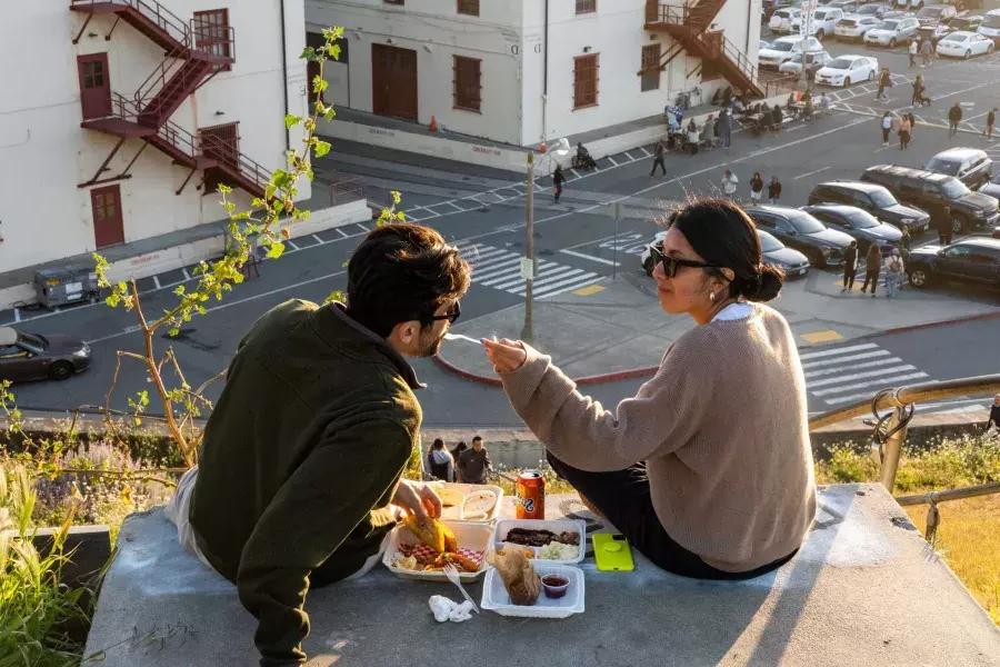 Una coppia cena all'aperto al Fort Mason Center di San Francisco. La donna dà al suo compagno un assaggio di cibo.