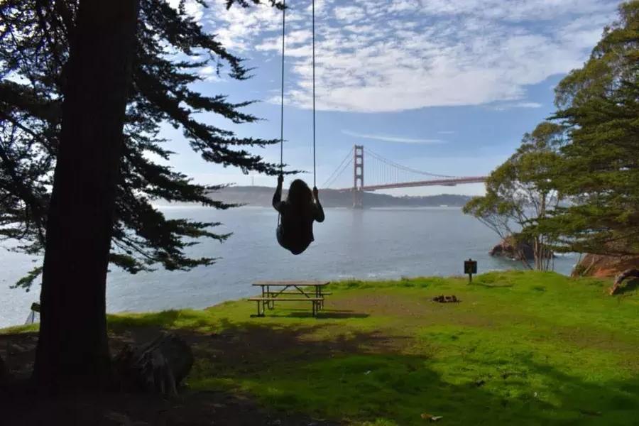 금문교가 내려다보이는 나무 그네에서 한 여성이 그네를 타고 있습니다. 샌프란시스코, 캘리포니아.