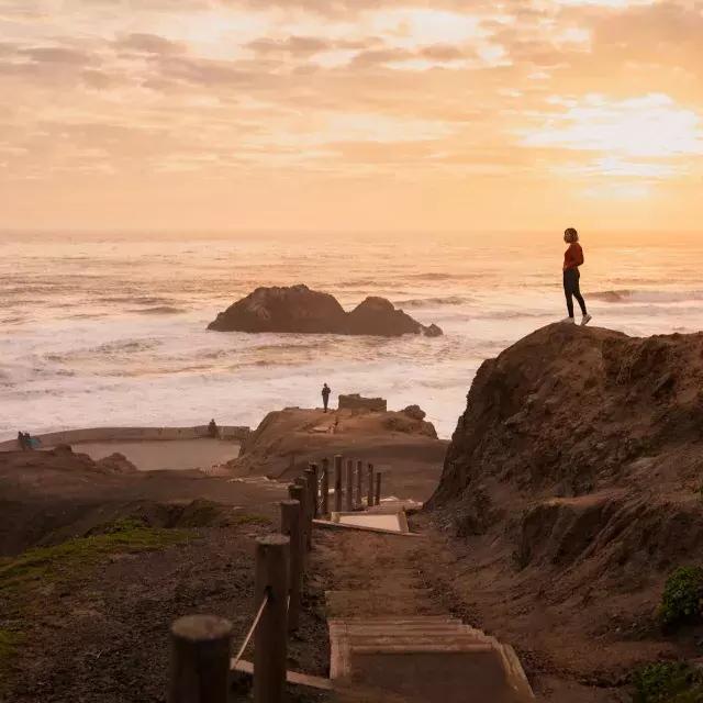 Dos personas se paran sobre rocas con vista al océano en Sutro Baths en San Francisco.