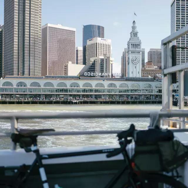 自行车靠在栏杆上，背景是渡轮大楼。.